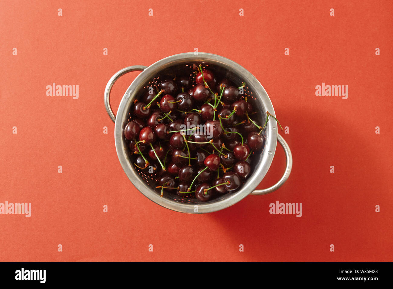 Summer ripe sweet cherry berries in a colander on a color background of the year 2019 Living Coral Pantone. Top view. Stock Photo