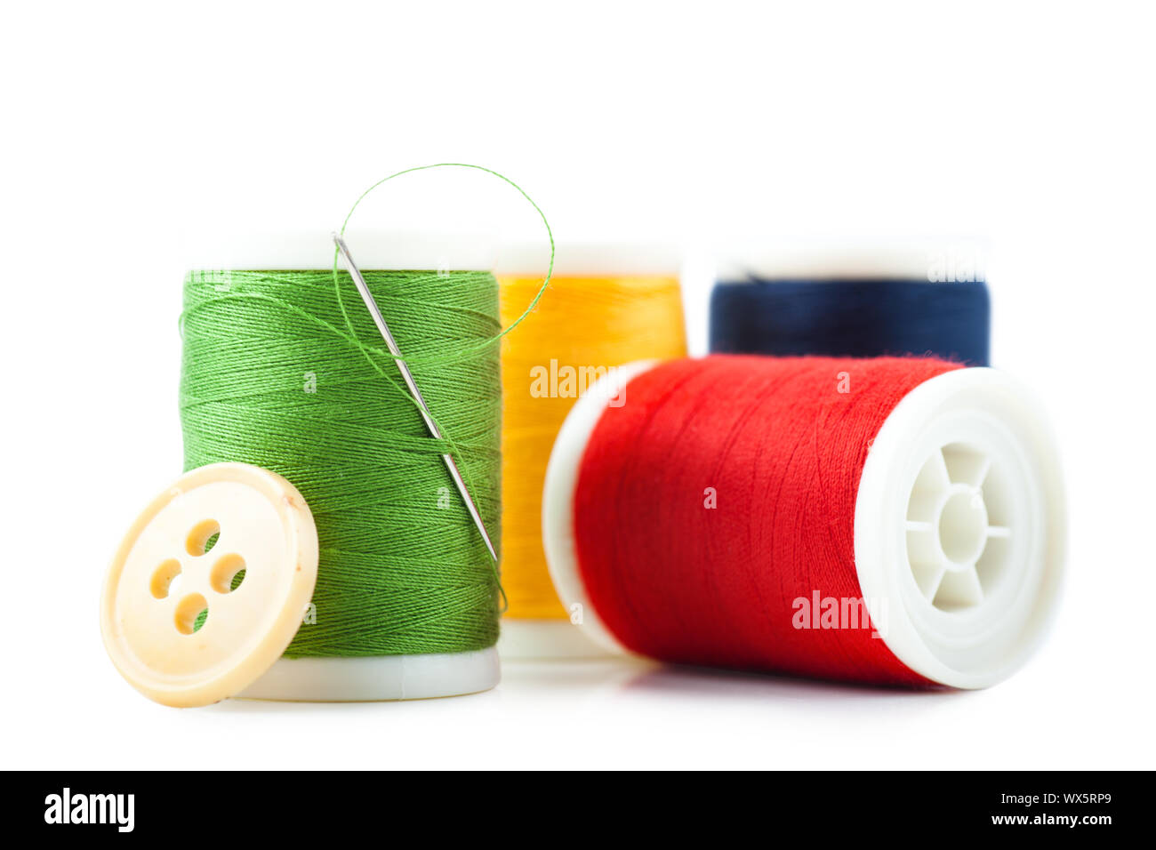 Four spools with green, red, yellow and blue threads, needle and button Stock Photo