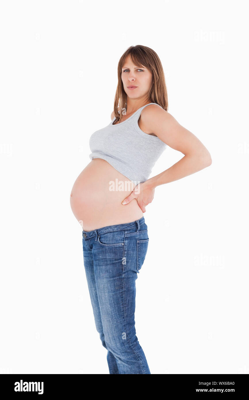 Beautiful pregnant woman holding her back while standing against a ...