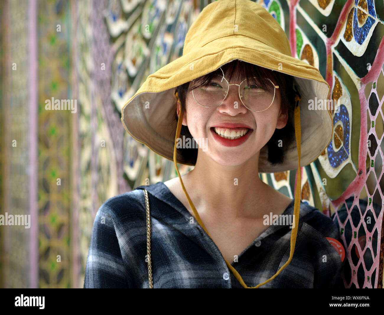 Young Chinese tourist poses for the camera in front of the mirror-patterned (wish-fulfilling) temple wall at Mandalay's Buddhist Su Taung Pyae Pagoda. Stock Photo