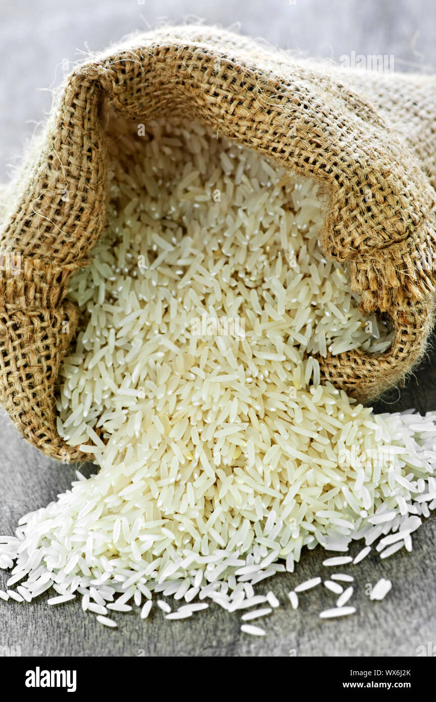 Raw long grain white rice grains in burlap bag Stock Photo