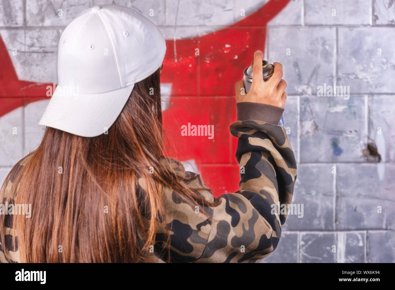 Teenage girl drawing graffiti with spray paint on street wall Stock