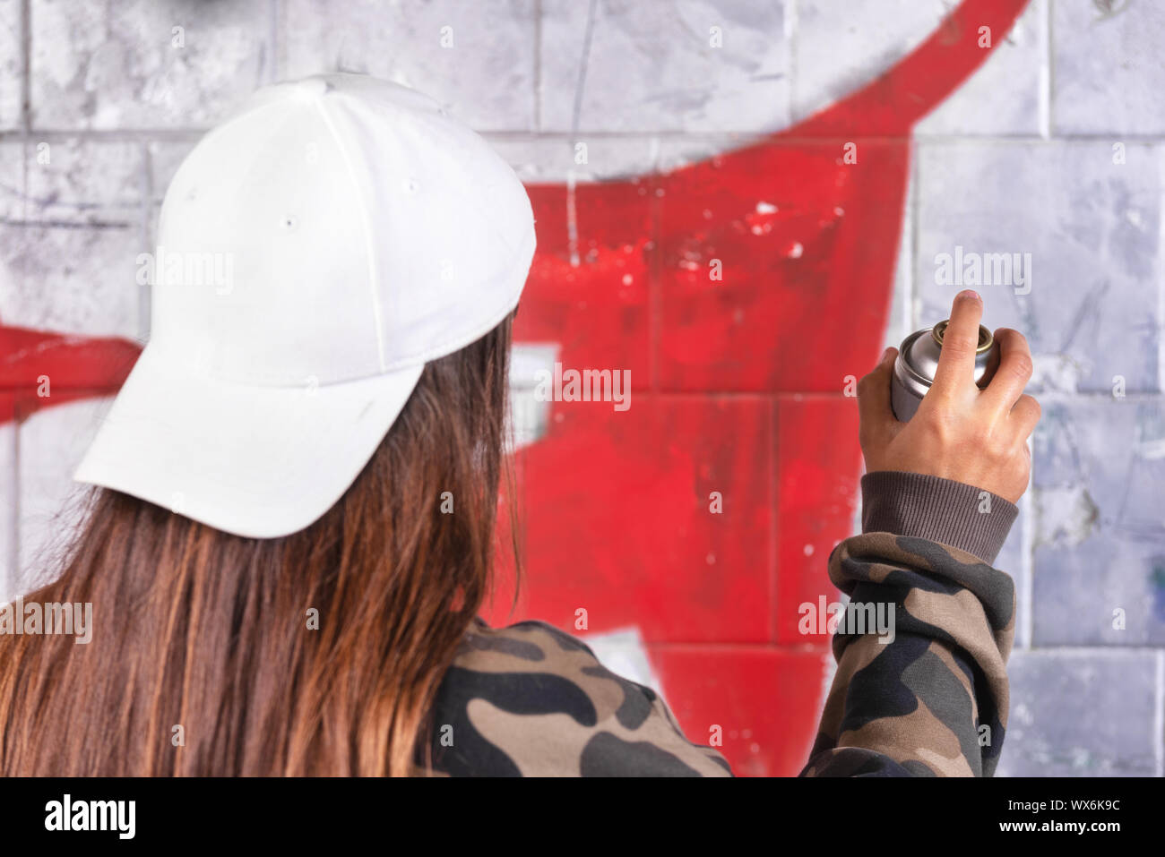 Teenage girl drawing graffiti with spray paint on street wall Stock