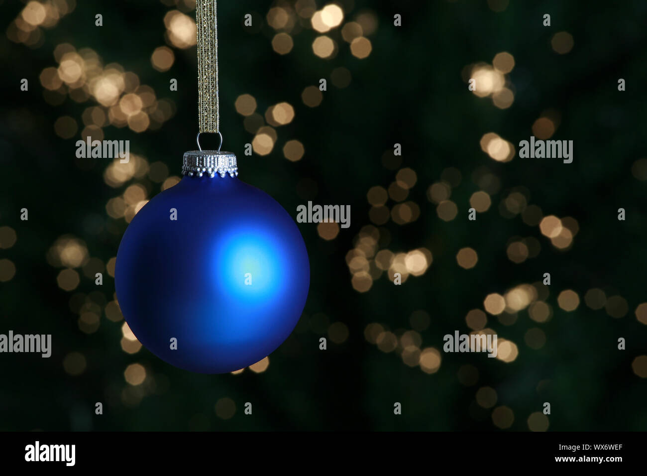Blue Christmas ornament hanging against lit Christmas tree Stock Photo ...
