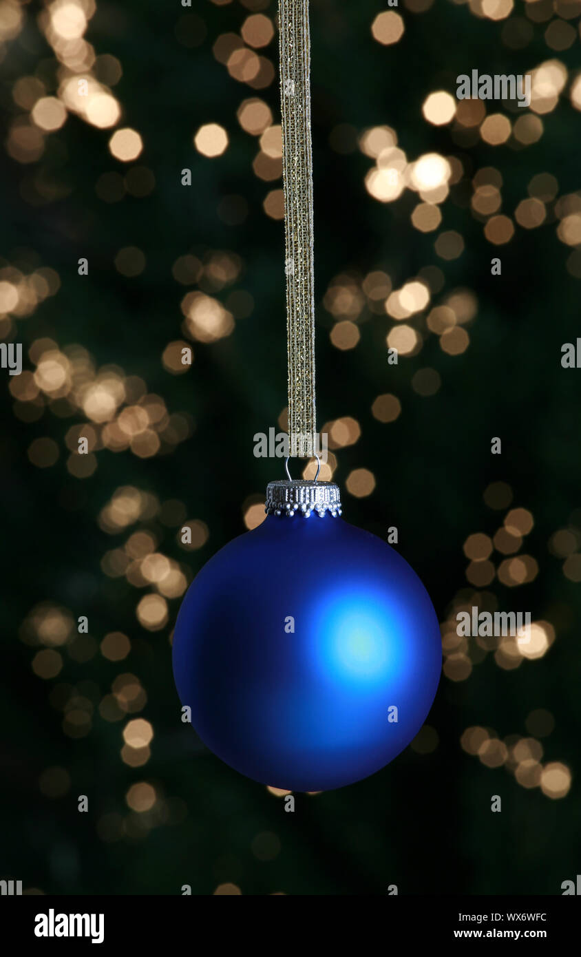 Blue Christmas ornament hanging against lit Christmas tree Stock Photo ...