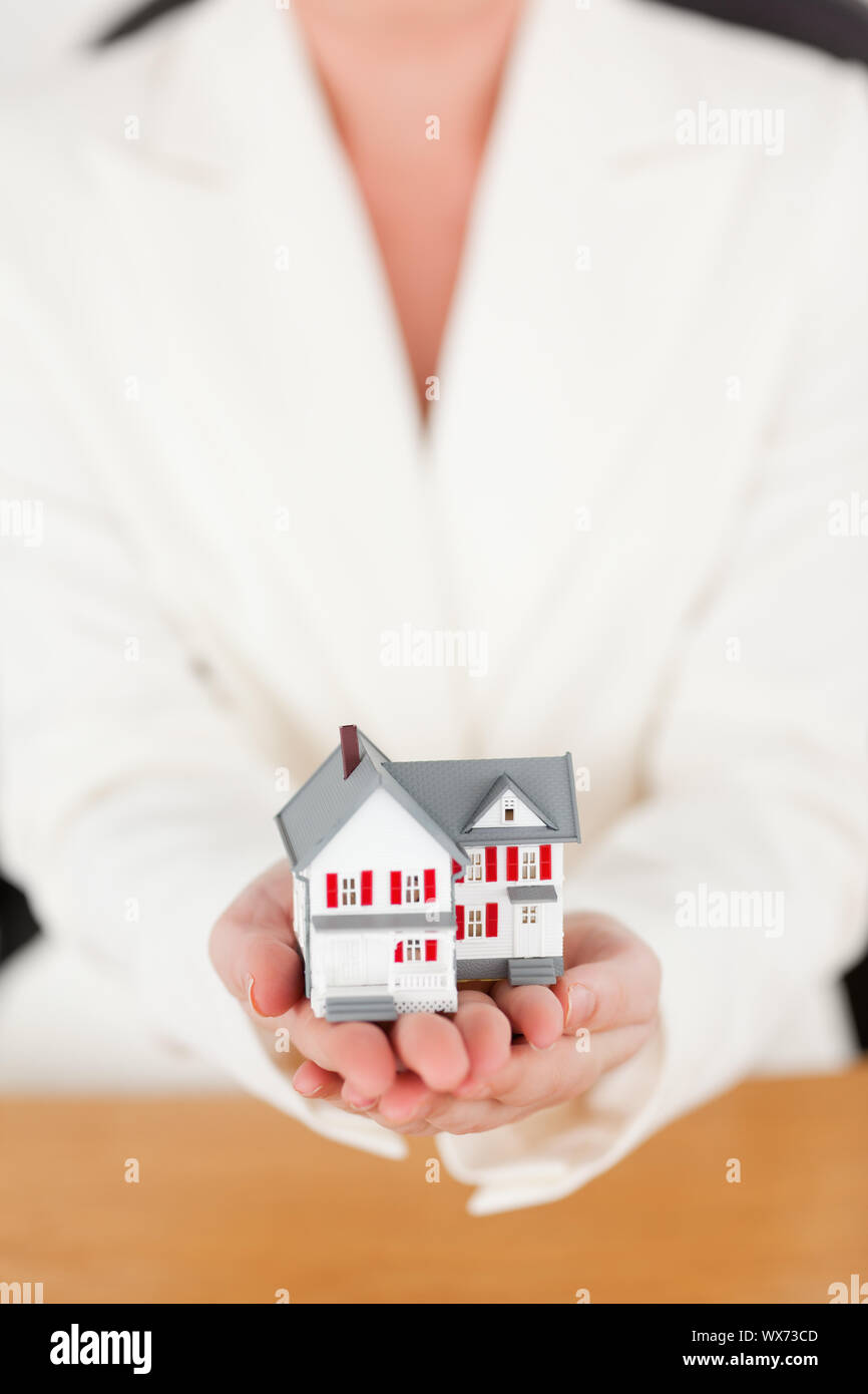 Young pretty red-haired female in suit holding a miniature house while ...