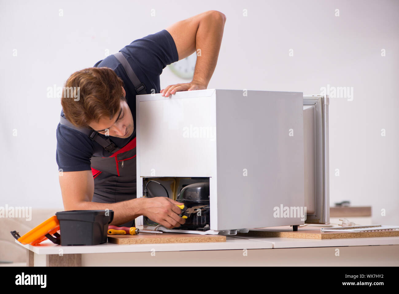 Young handsome contractor repairing fridge Stock Photo