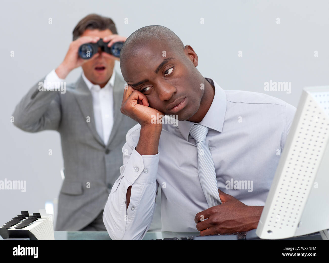 Afro-amercian businessman annoyed by a man looking through binoculars in the office Stock Photo