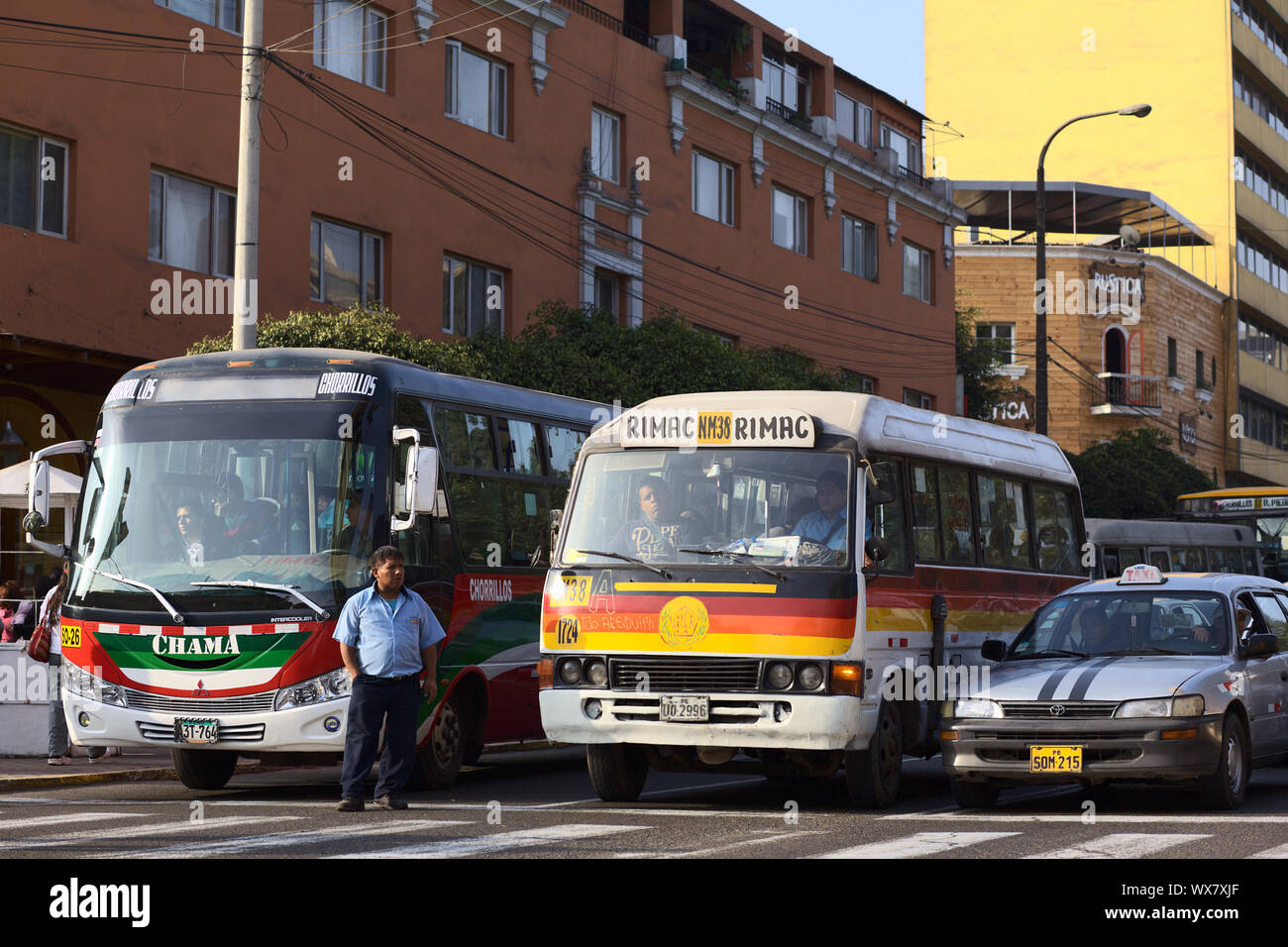 LIMA, PERU - SEPTEMBER 13, 2011: Buses and a taxi standing at red light with a bus conductor standing on Avenida Diagonal calling out for passengers Stock Photo