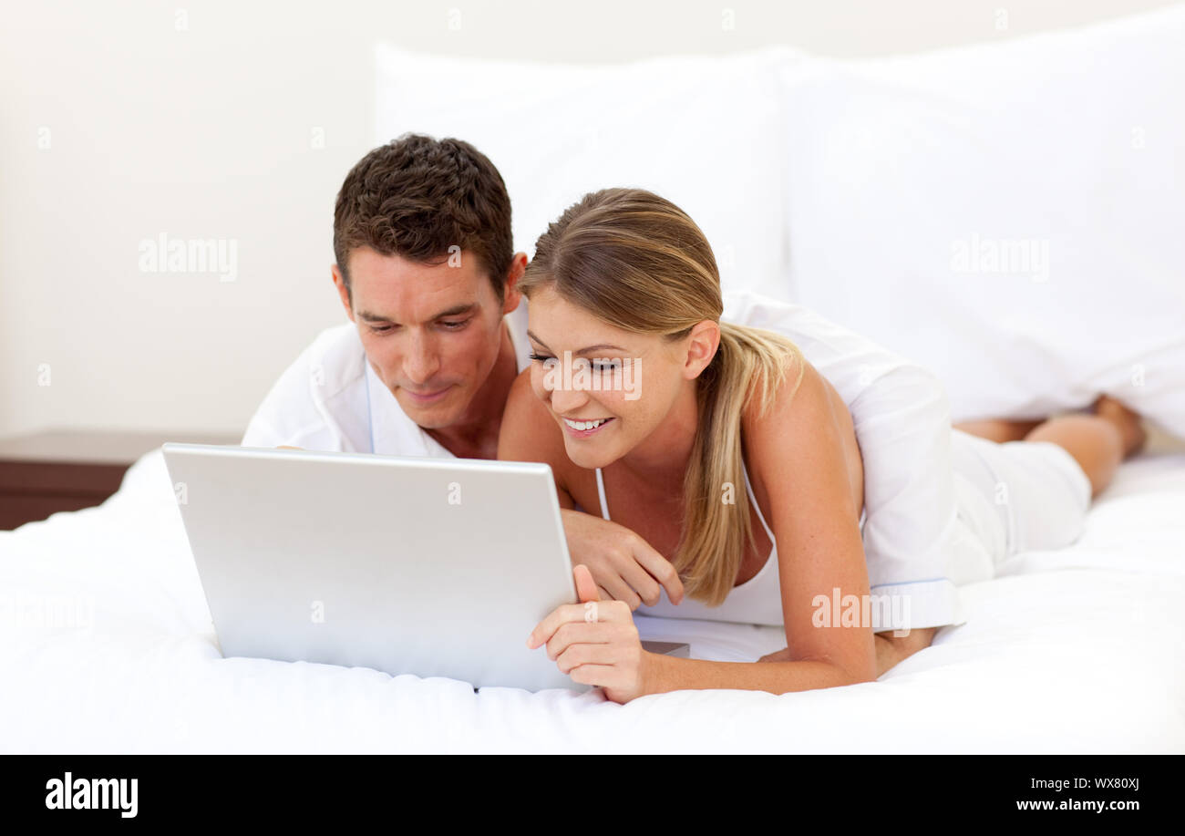 Smiling couple using a laptop lying on their bed Stock Photo - Alamy