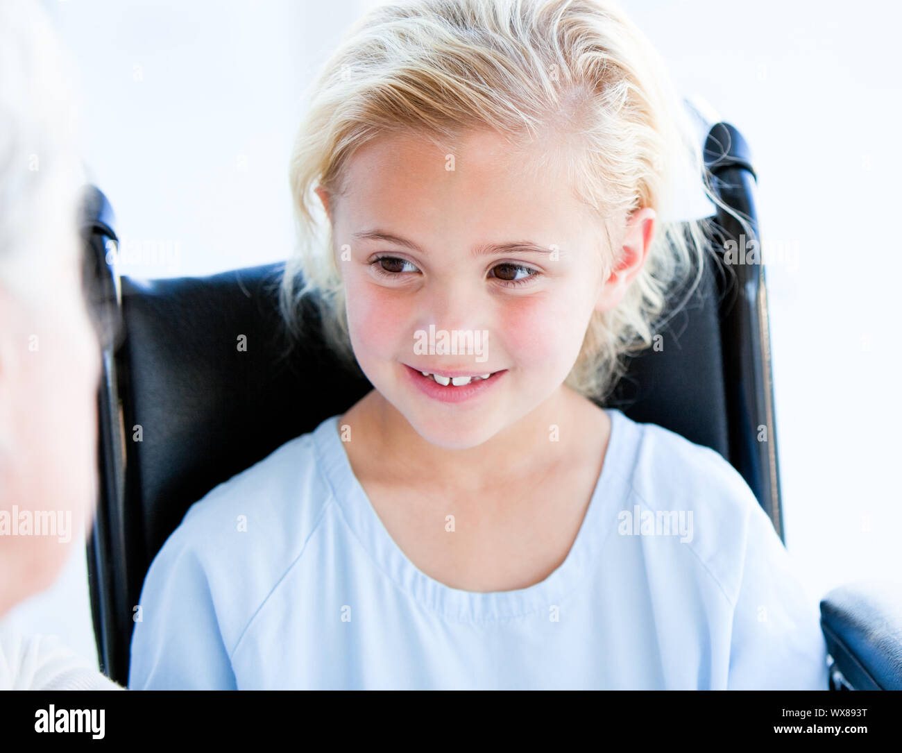 Blond little girl sitting on a wheelchair in a hospital Stock Photo
