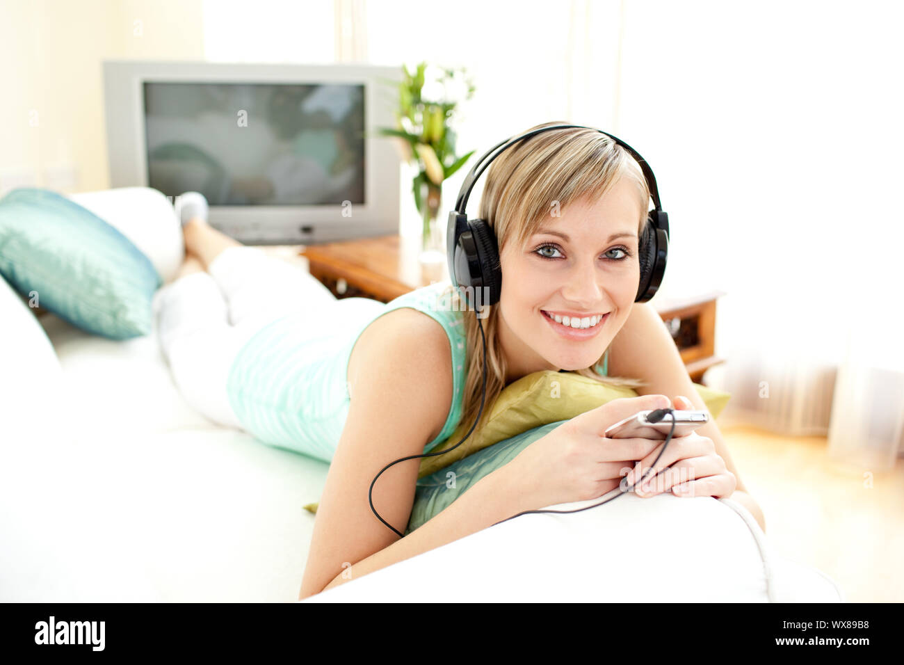 Cheerful blond woman listening music lying on a sofa in the living-room ...