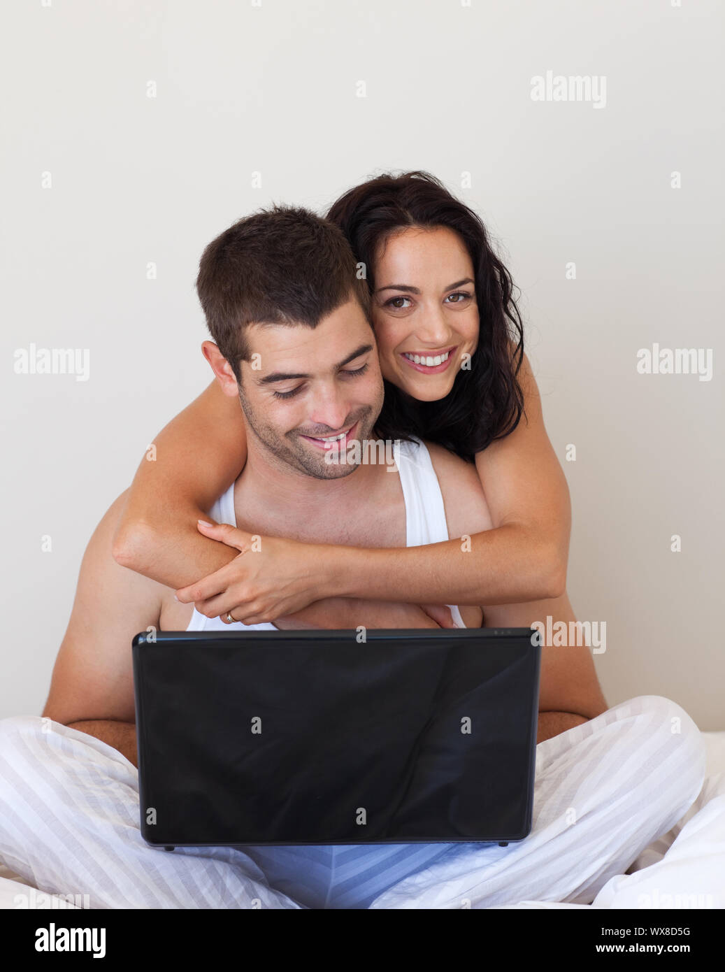 Smiling couple using a laptop sitting on a bed Stock Photo - Alamy