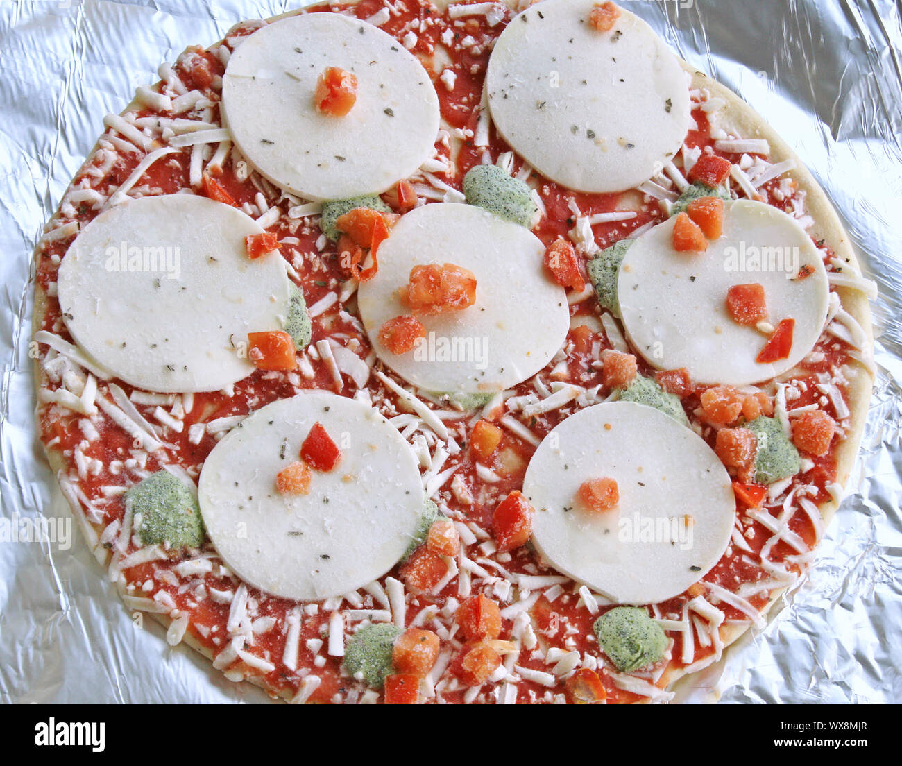 Frozen thin crust pizza with mozzarella cheese and veggies on aluminum foil ready for cooking Stock Photo