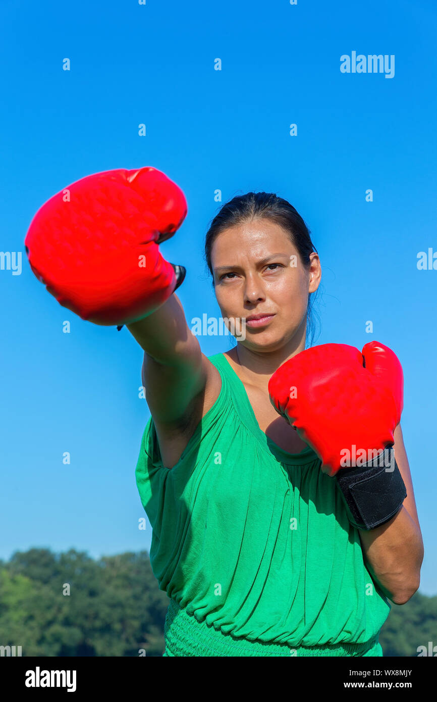 Young woman punches with red boxing gloves outside Stock Photo