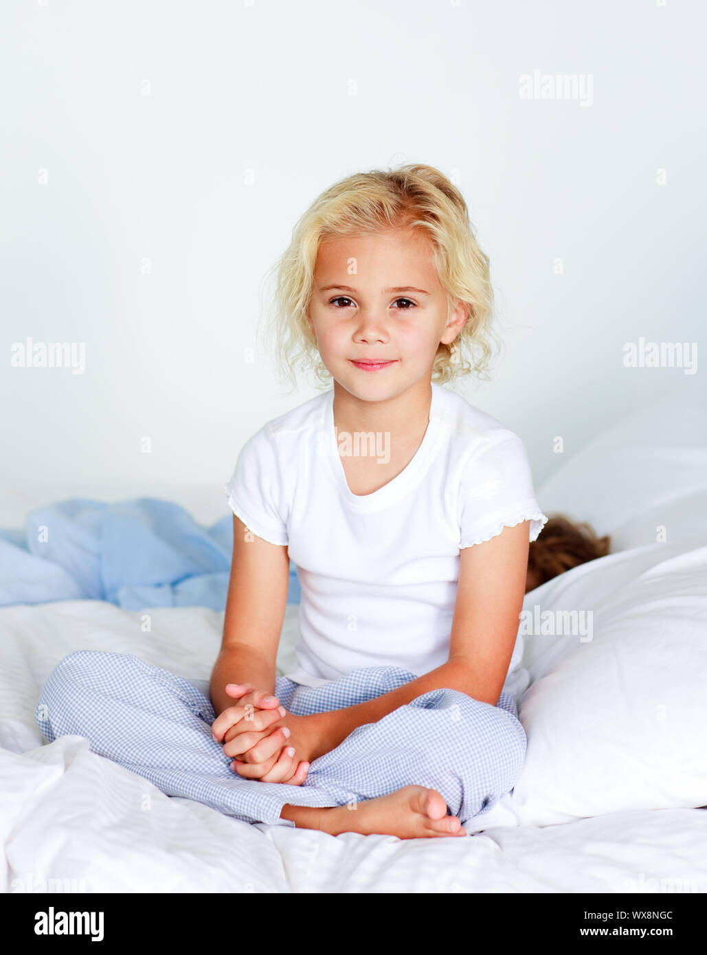 Cute little blond girl sitting on her bed looking at the camera Stock