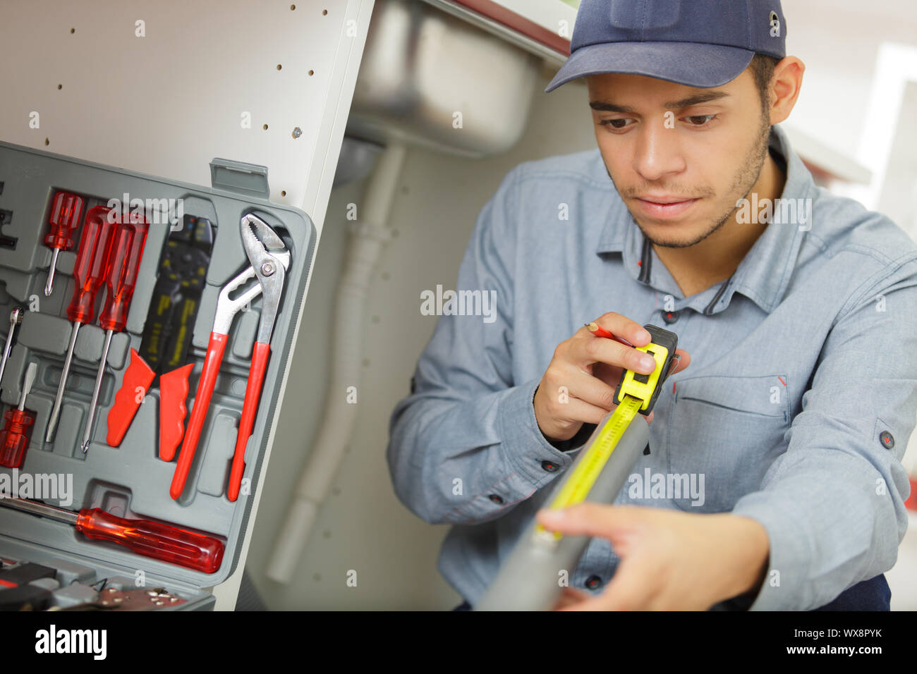 young tradesman using tape measure to measure waste pipe Stock Photo