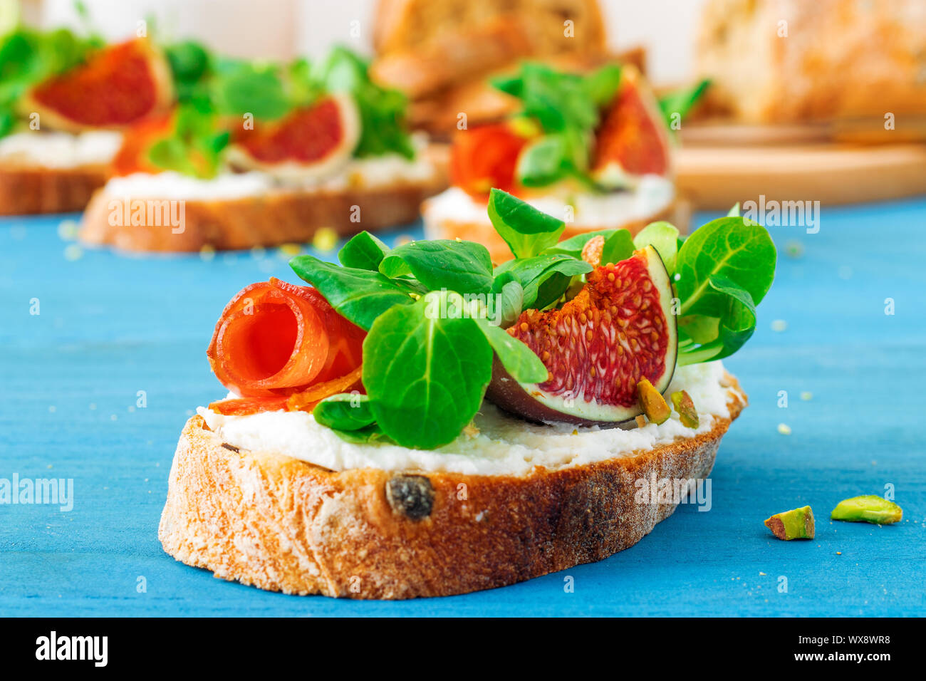 Toast from swiss twisted bread, with feta cheese or ricotta, fresh figs, rolled slice of bacon, fresh leaves of corn or valerian salad and crushed pis Stock Photo