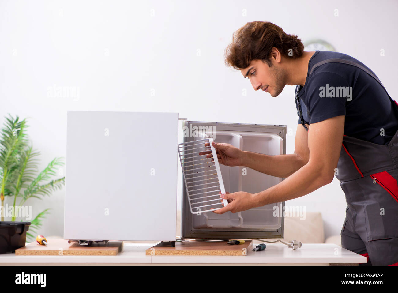 Young handsome contractor repairing fridge Stock Photo