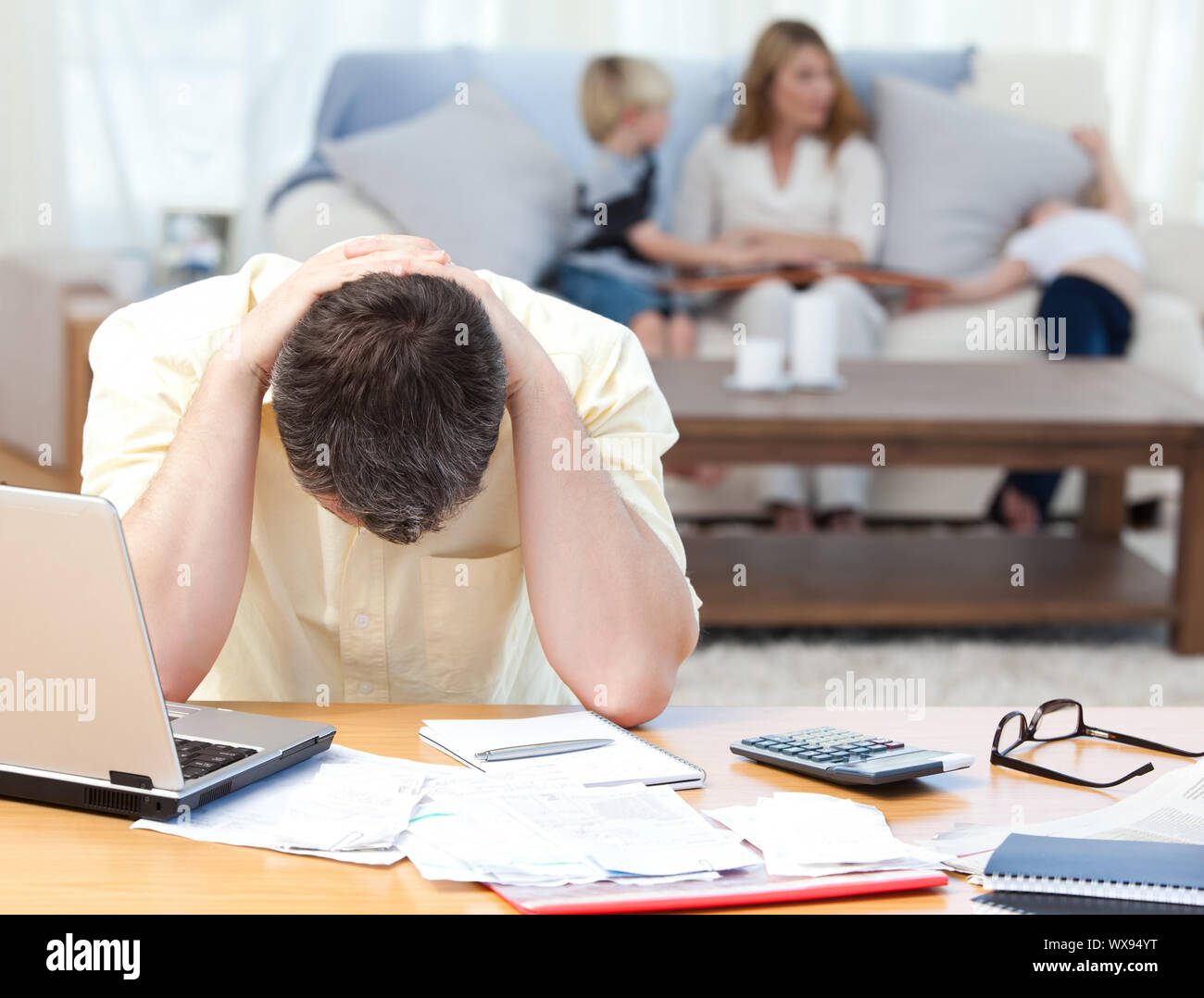 Man calculating his bills while his family are on the sofa Stock Photo