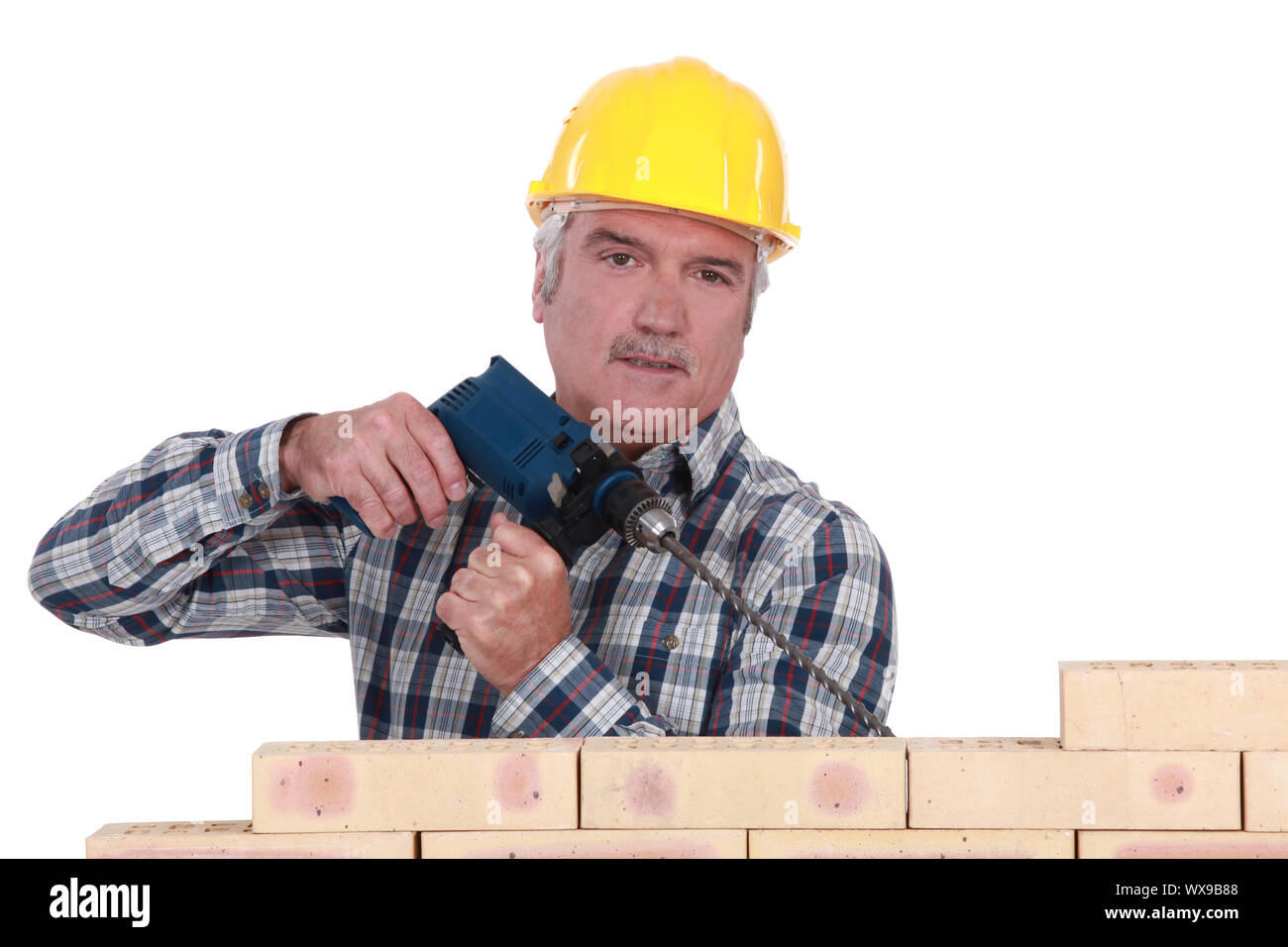 Grey-haired builder drilling into wall Stock Photo