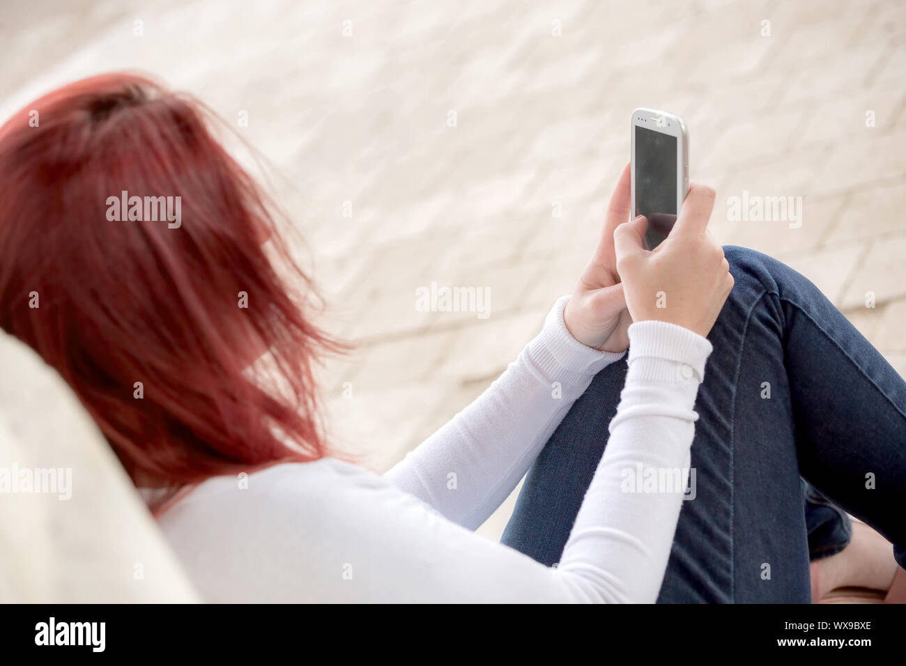 Pretty smiling redhead woman sending messages on her cell phone in a park. . Focus on her phone Stock Photo