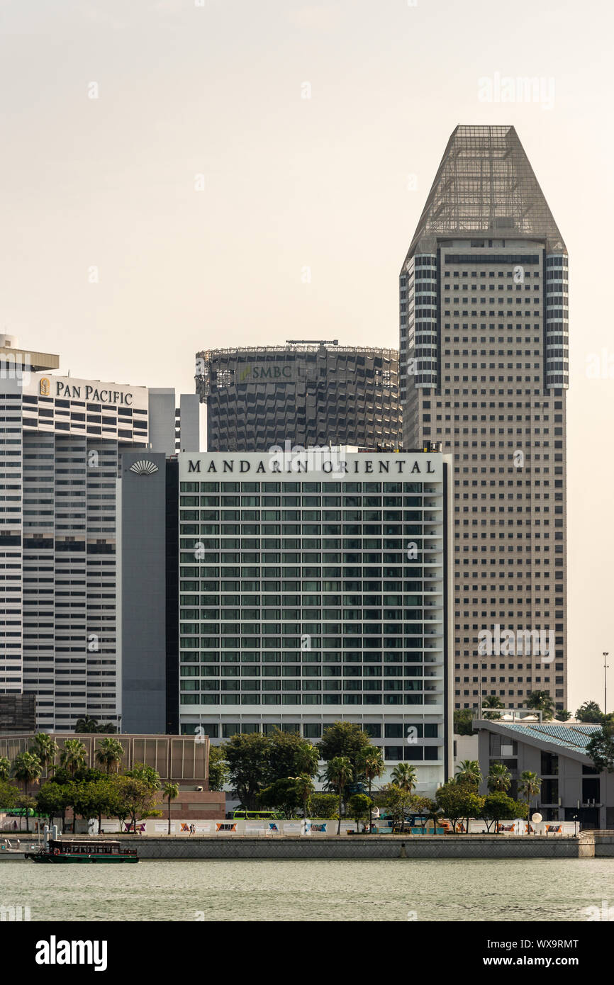 Singapore - March 21, 2019: Four tall buildings at Marina Bay include Mandarin Oriental, SMBC and Pan Pacific under sliver sky. Water up front. Stock Photo