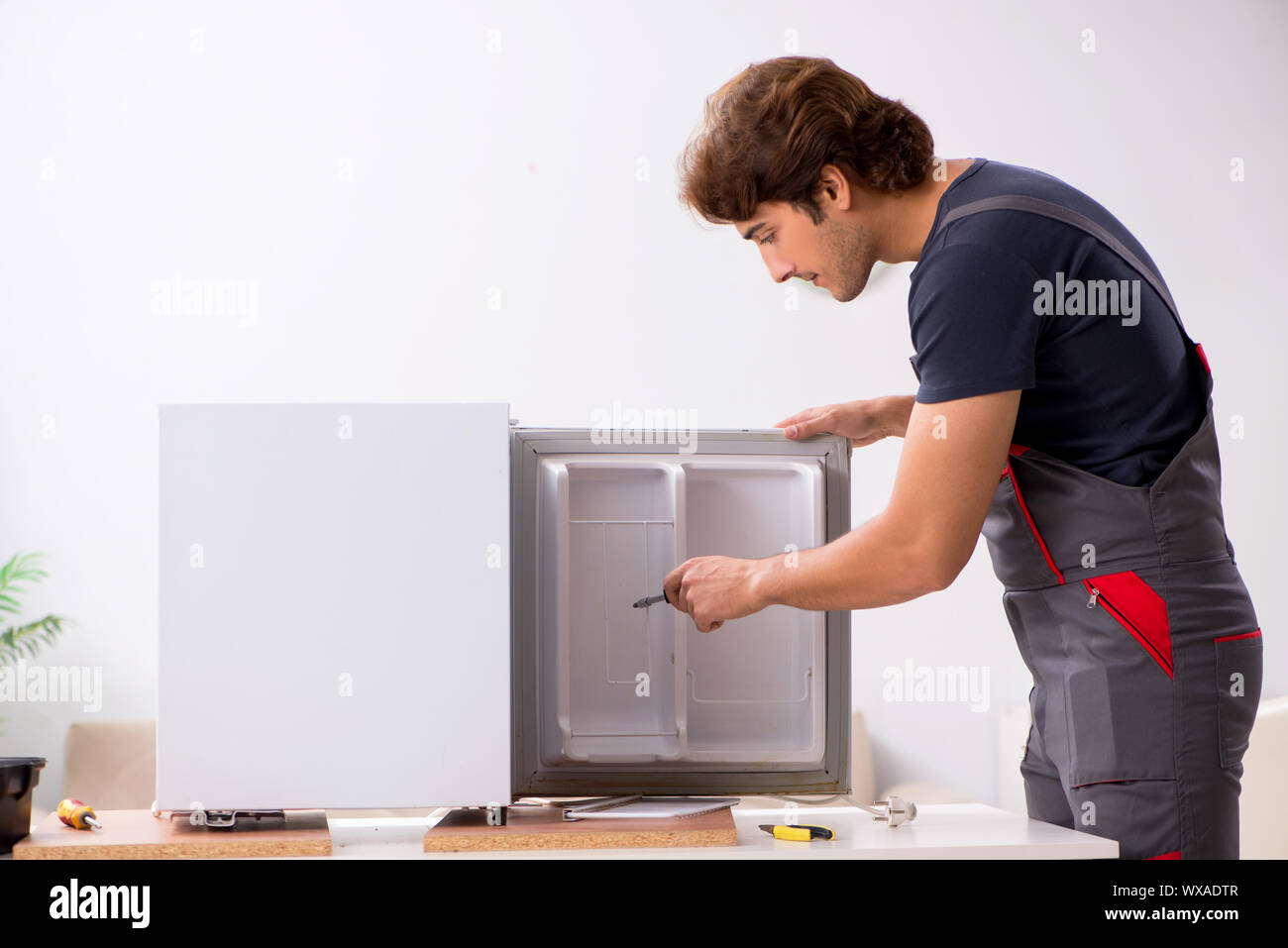 Young handsome contractor repairing fridge Stock Photo