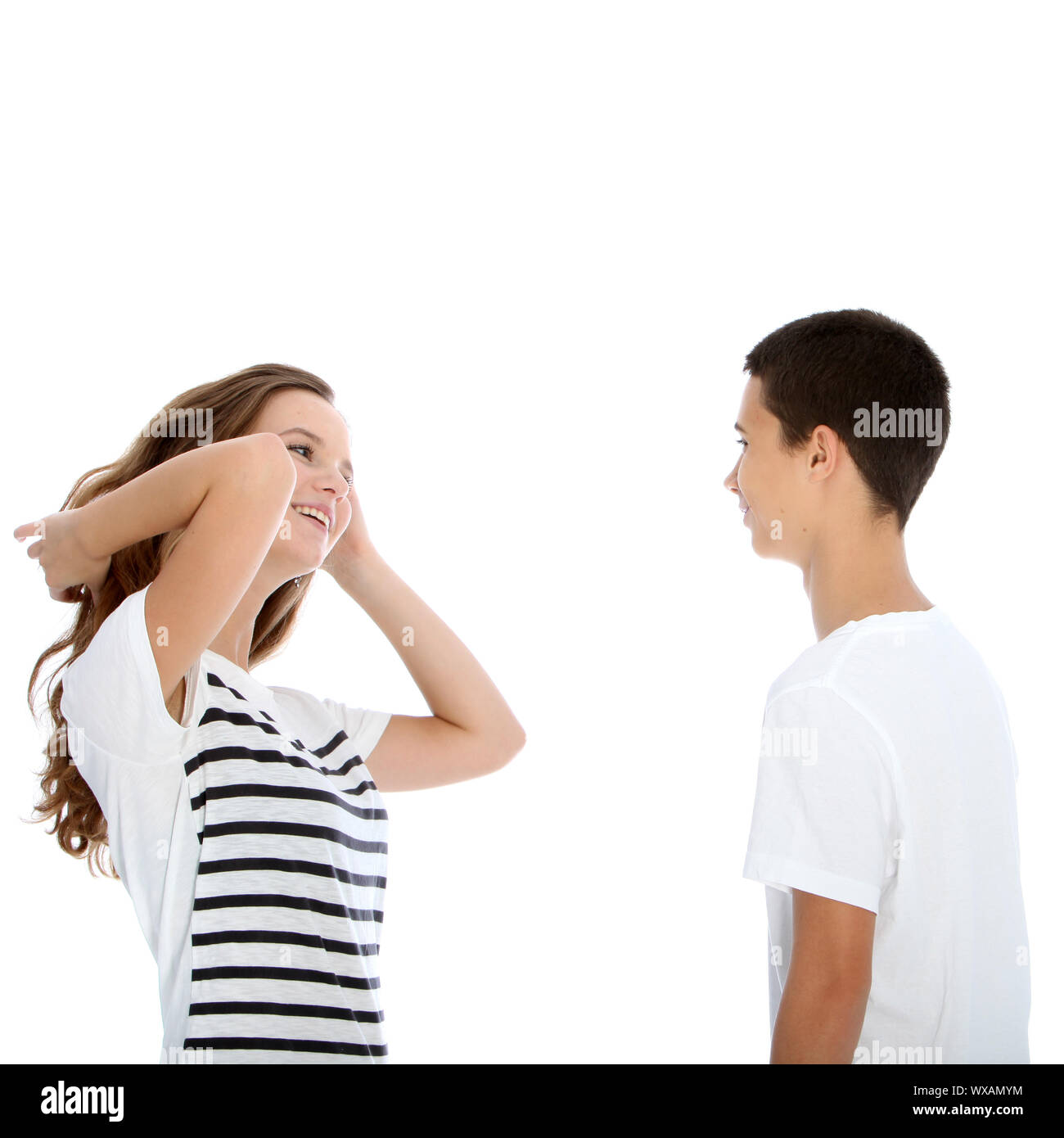 Young teenage couple talking with the girl flicking her hair and laughing flirtaceously isolated on white Stock Photo