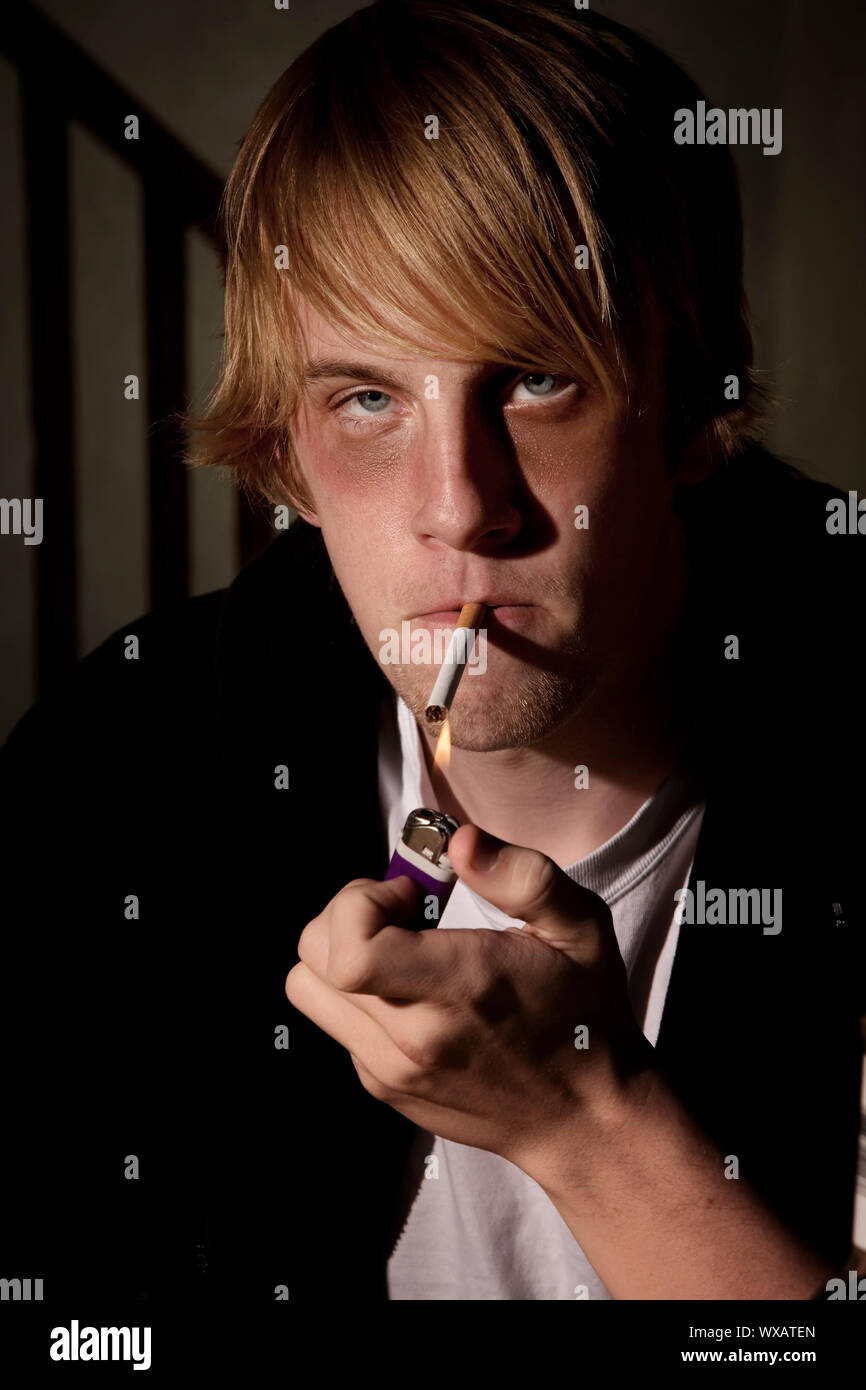 Depressed young man smoking in a tenement hovel Stock Photo