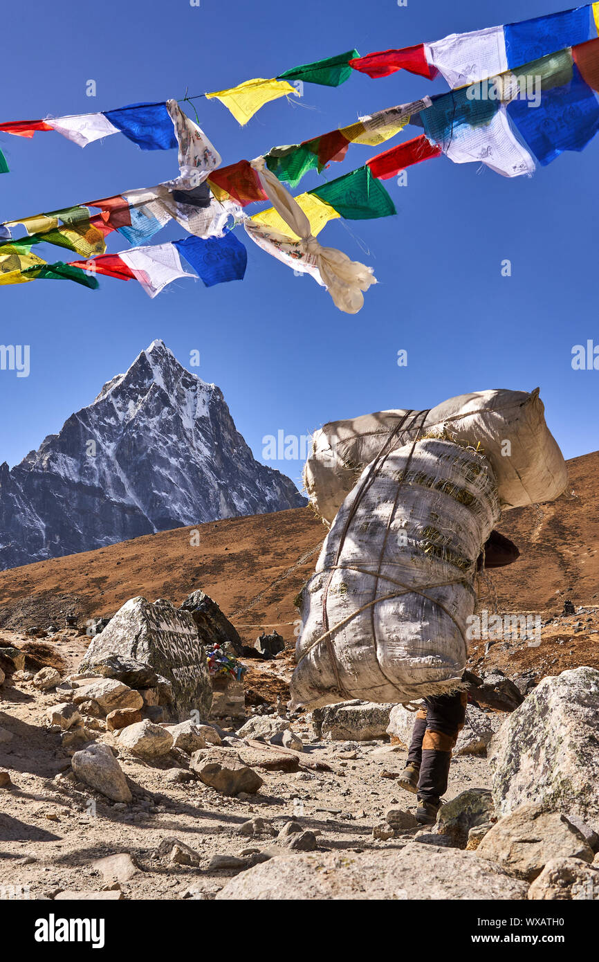 Porter with Mountain Cholatse and prayer flags in Nepal Stock Photo