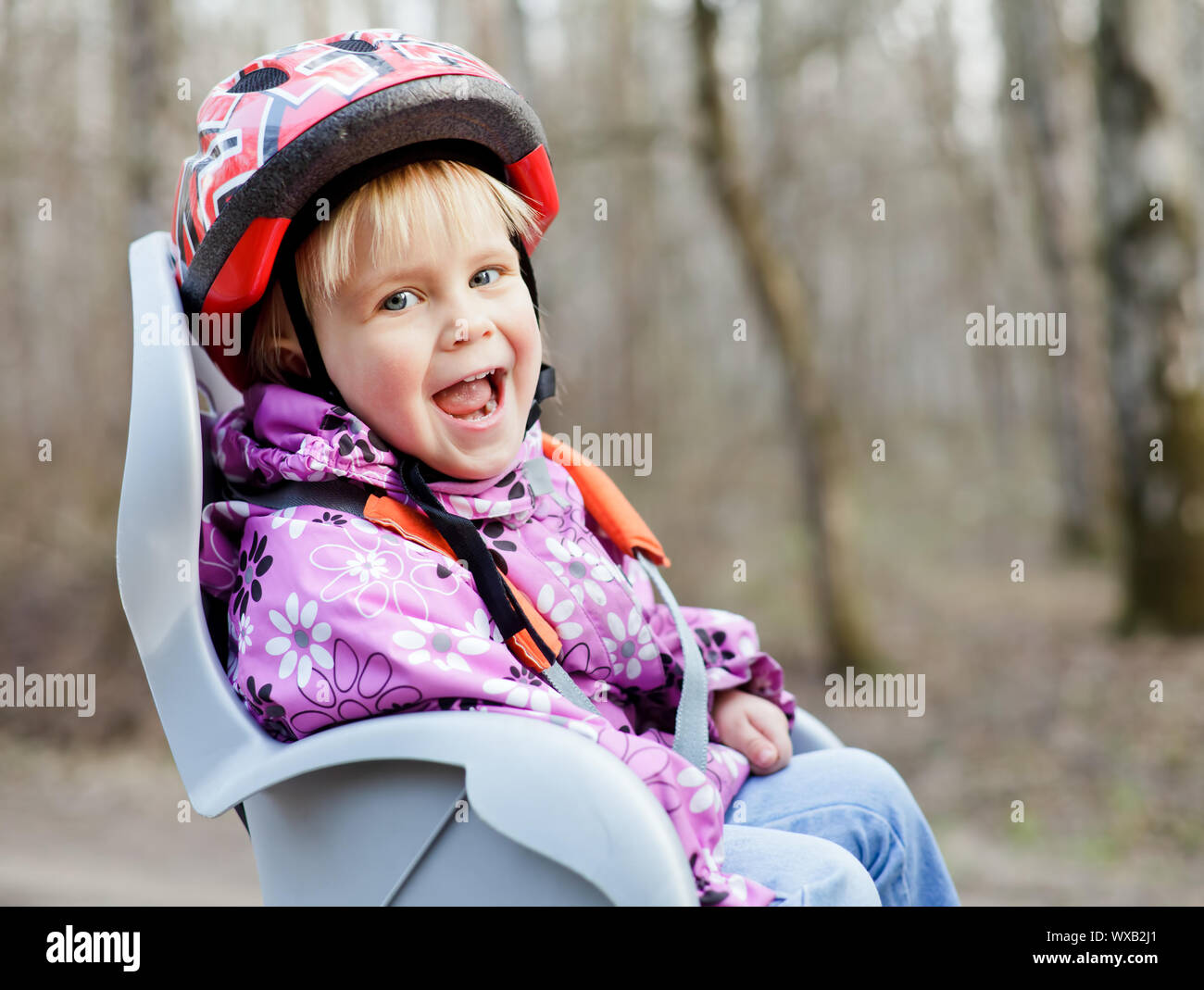 Happy little girl wearing helmet sitting in bycicle child seat Stock