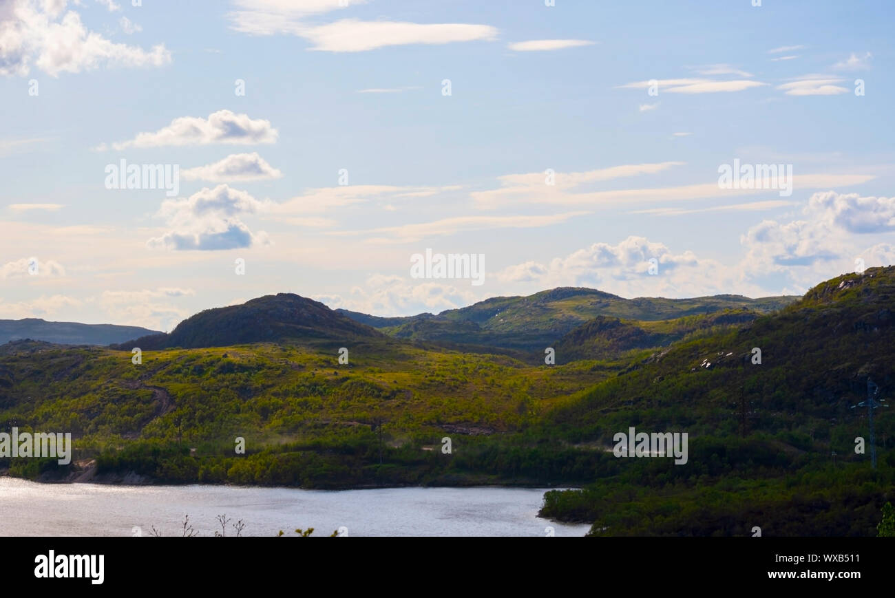 Green hills under a low, deep Northern sky and peacefull lake. These places in the Murmansk region are not far from Teriberka. Clouds fly over the tre Stock Photo