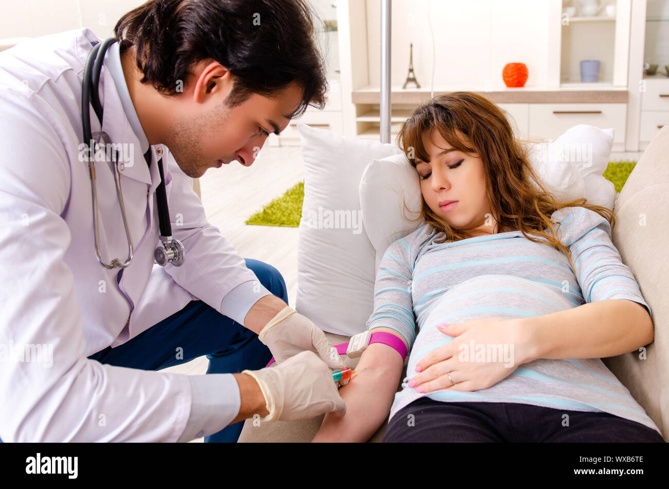 Young handsome doctor visiting pregnant woman at home Stock Photo