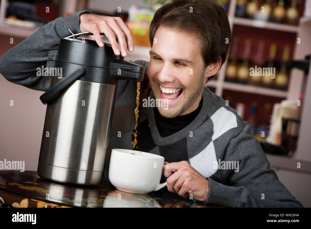 Young man crazily pouring coffee from a thermos in a cafe Stock Photo