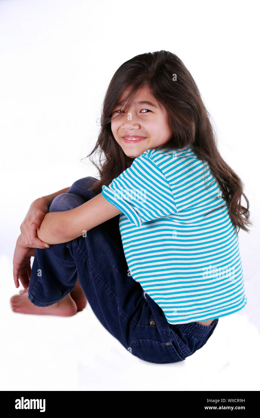 Happy little girl sitting with arms around knees, part asian