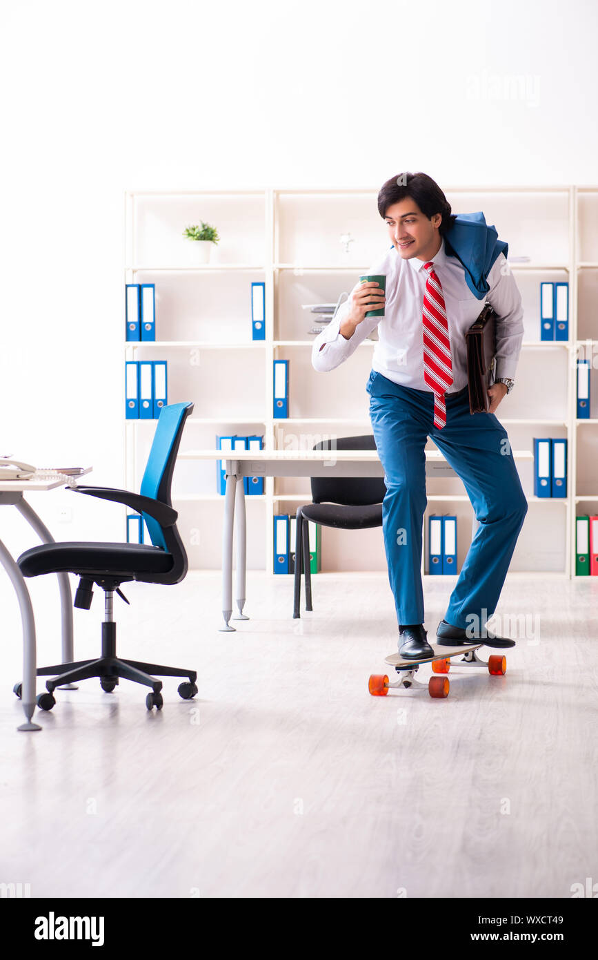 Young handsome businessman with longboard in the office Stock Photo