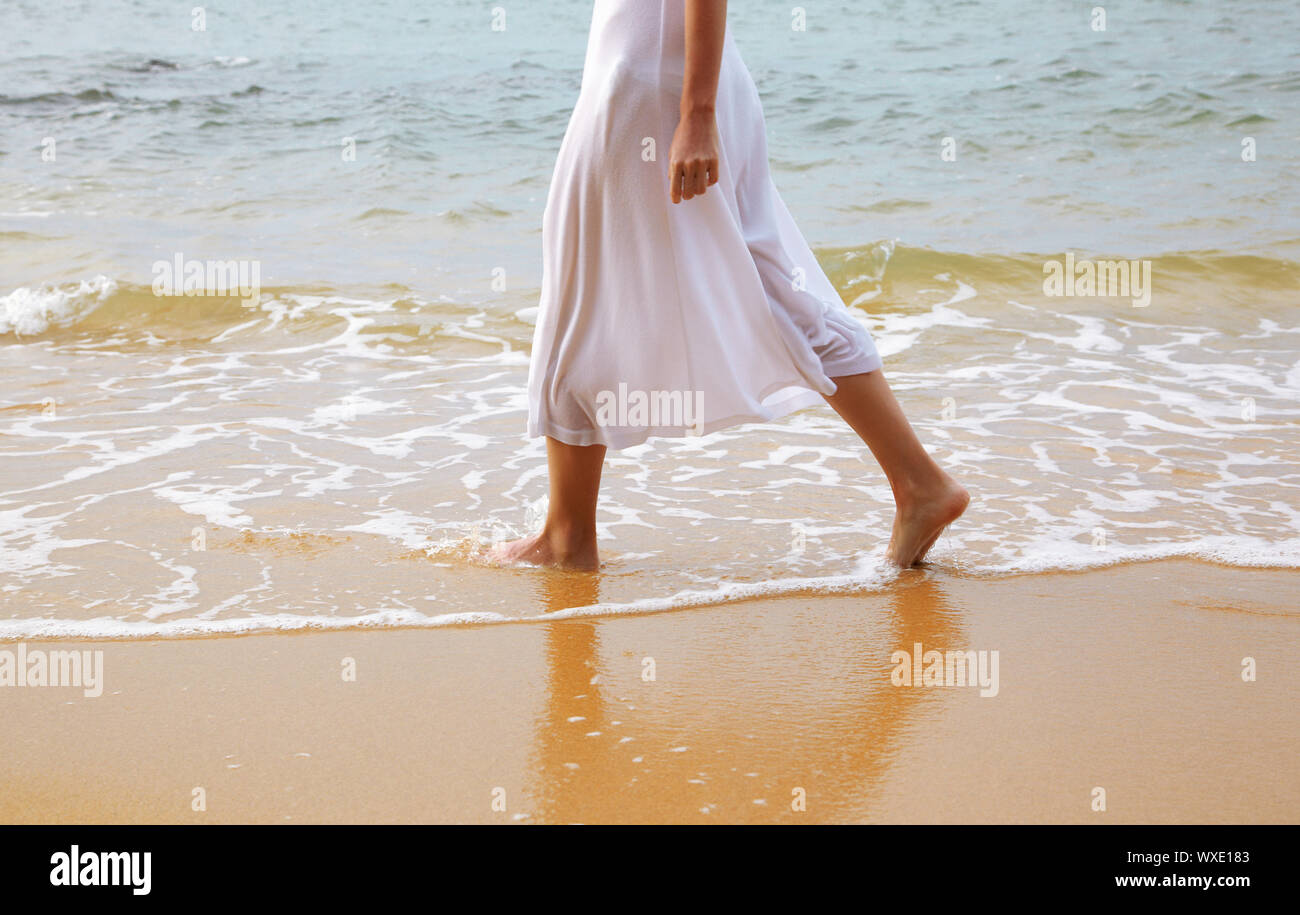 body part outdoor portrait of young woman's legs in white cotton skirt walking in coastal waves at the beach of Phuket island, Thailand Stock Photo