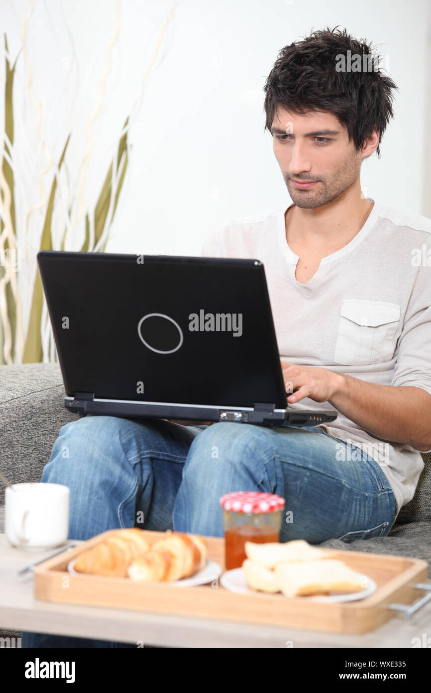 Man having breakfast whilst using laptop Stock Photo