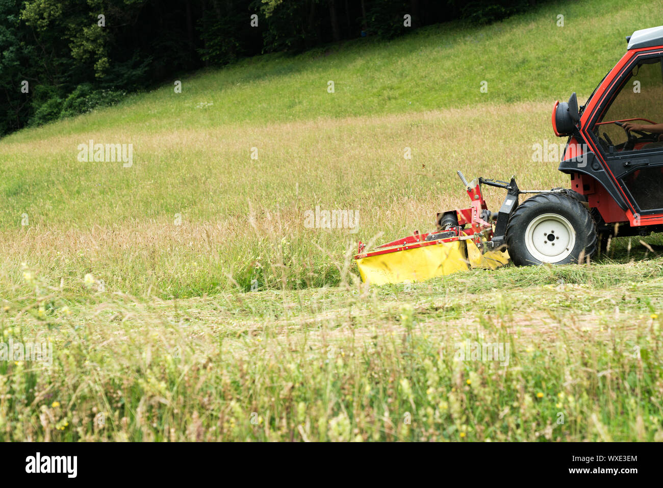 small tractor with mower in front cutting a steep hillside wildflower