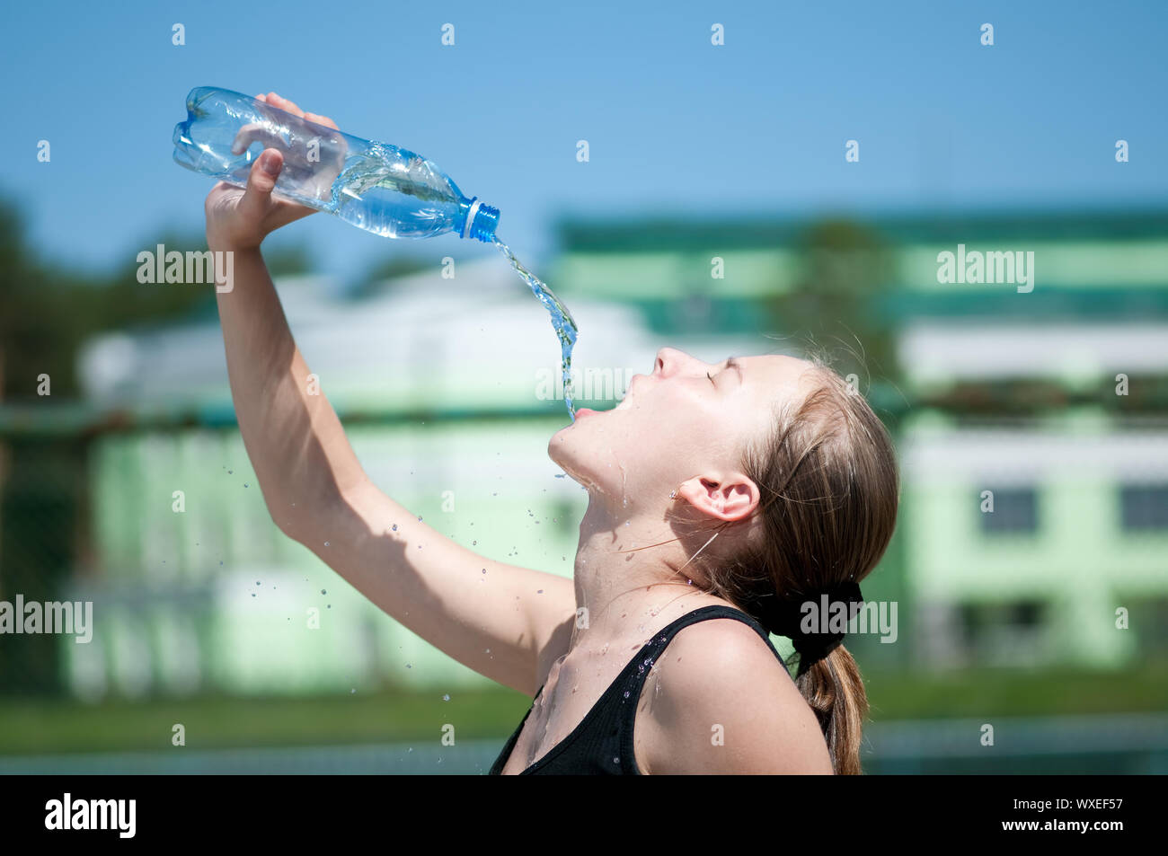 Beautiful young woman drinking water after exercise on sunny summer day
