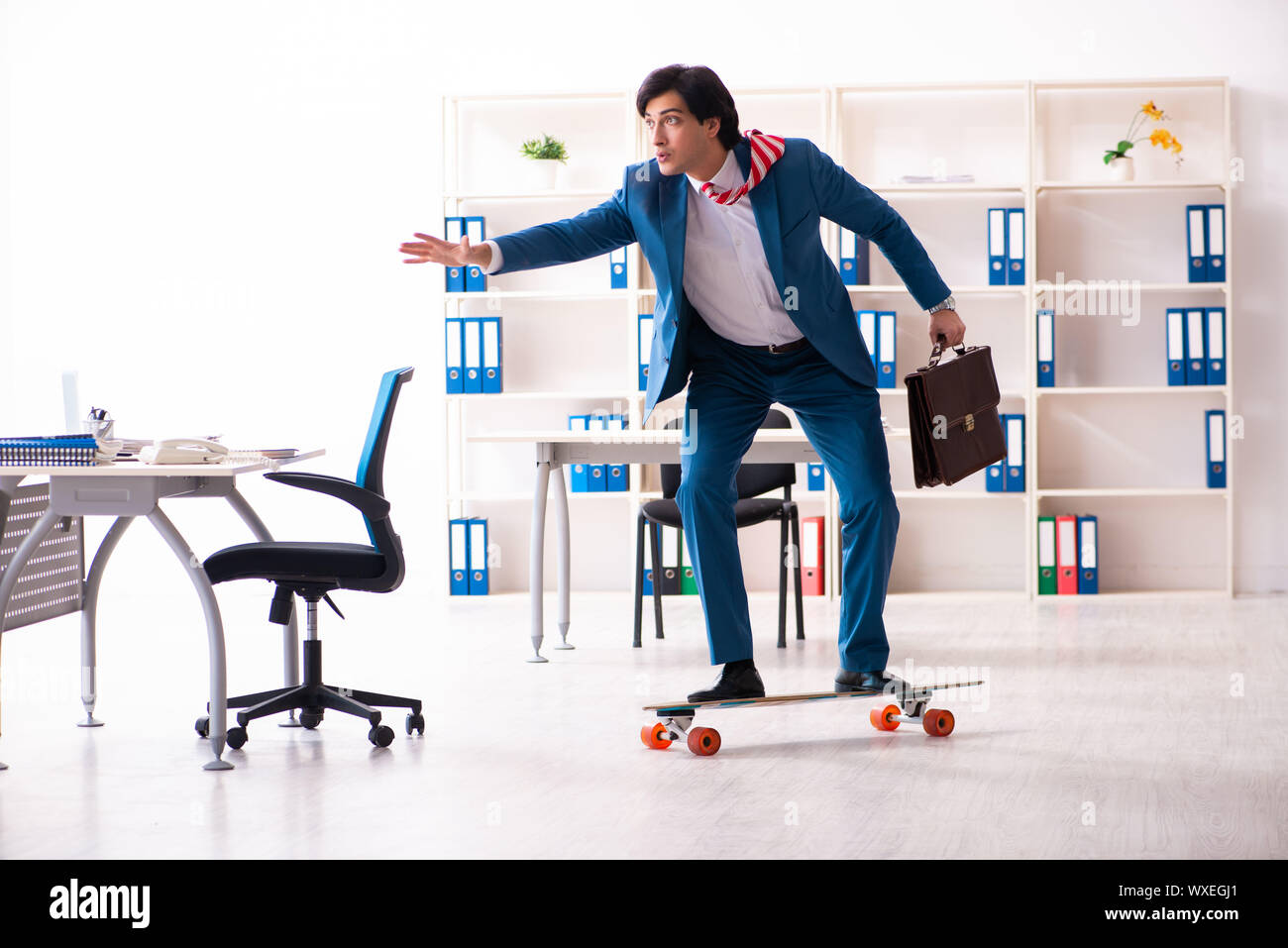 Young handsome businessman with longboard in the office Stock Photo