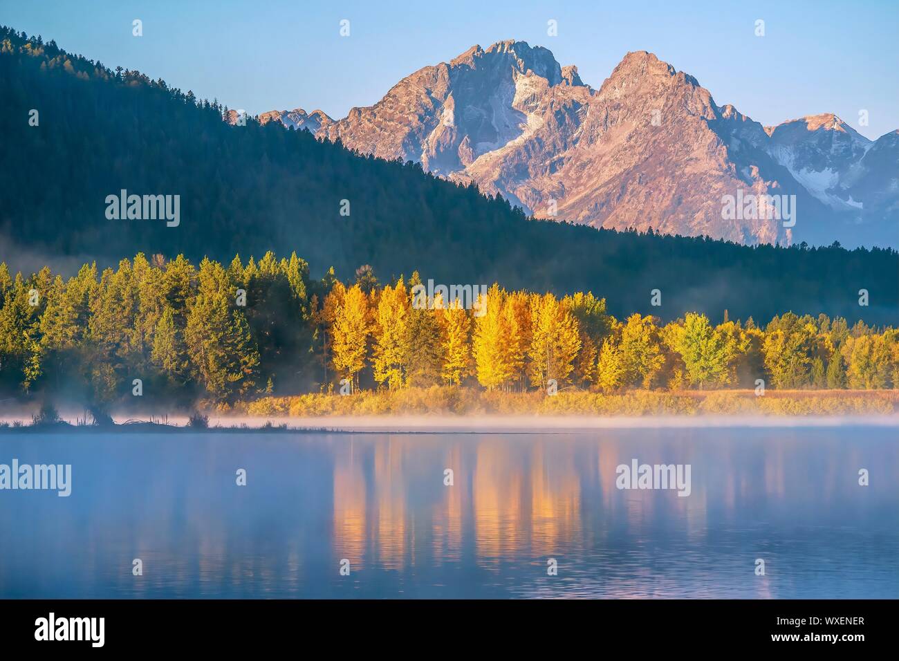 Grand Teton National Park, with mist on the water, colorful aspen trees, evergreen forest, and the craggy Teton mountain range. Stock Photo