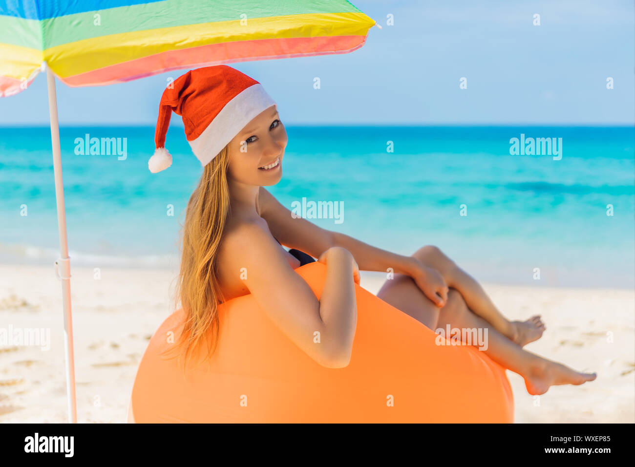 Woman on an inflatable beach couch and Christmas hat on the beach under an umbrella Stock Photo