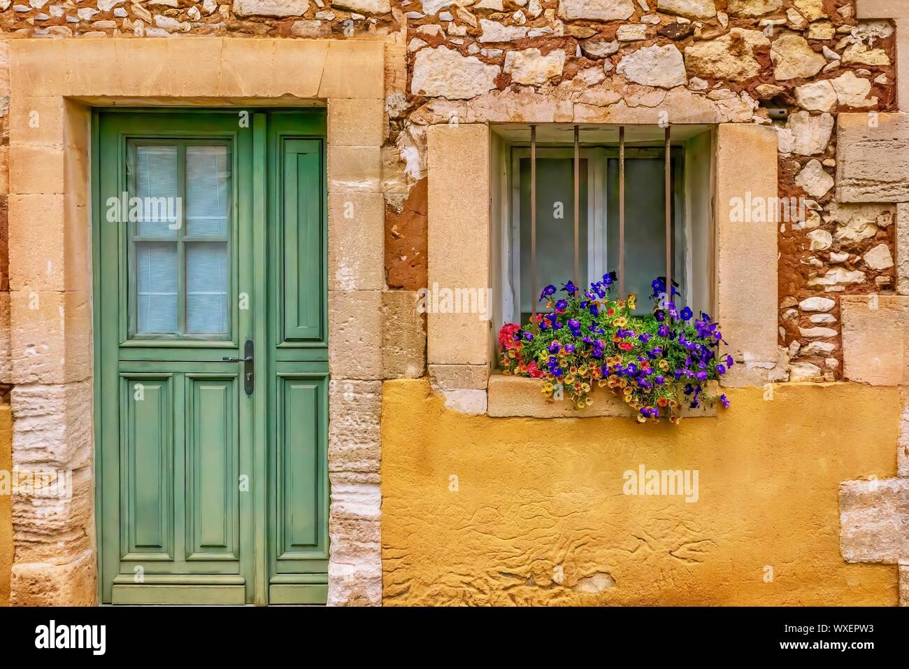Street view of an old house facade in Provence, where a layer of locally mined ochre has been partially removed from the stone wall underneath. Roussi Stock Photo