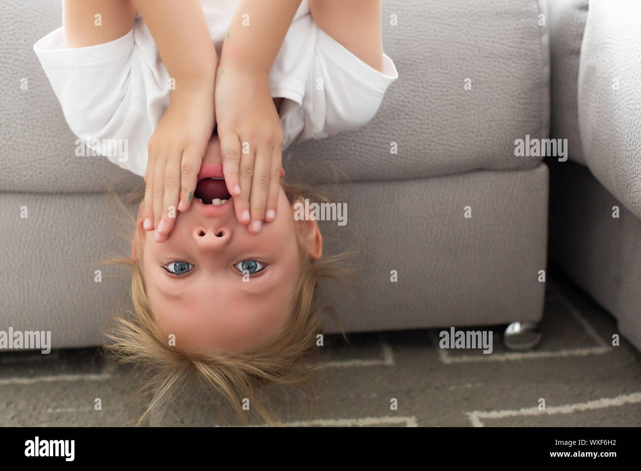 Amused funny girl hanging upside down on couch at home Stock Photo