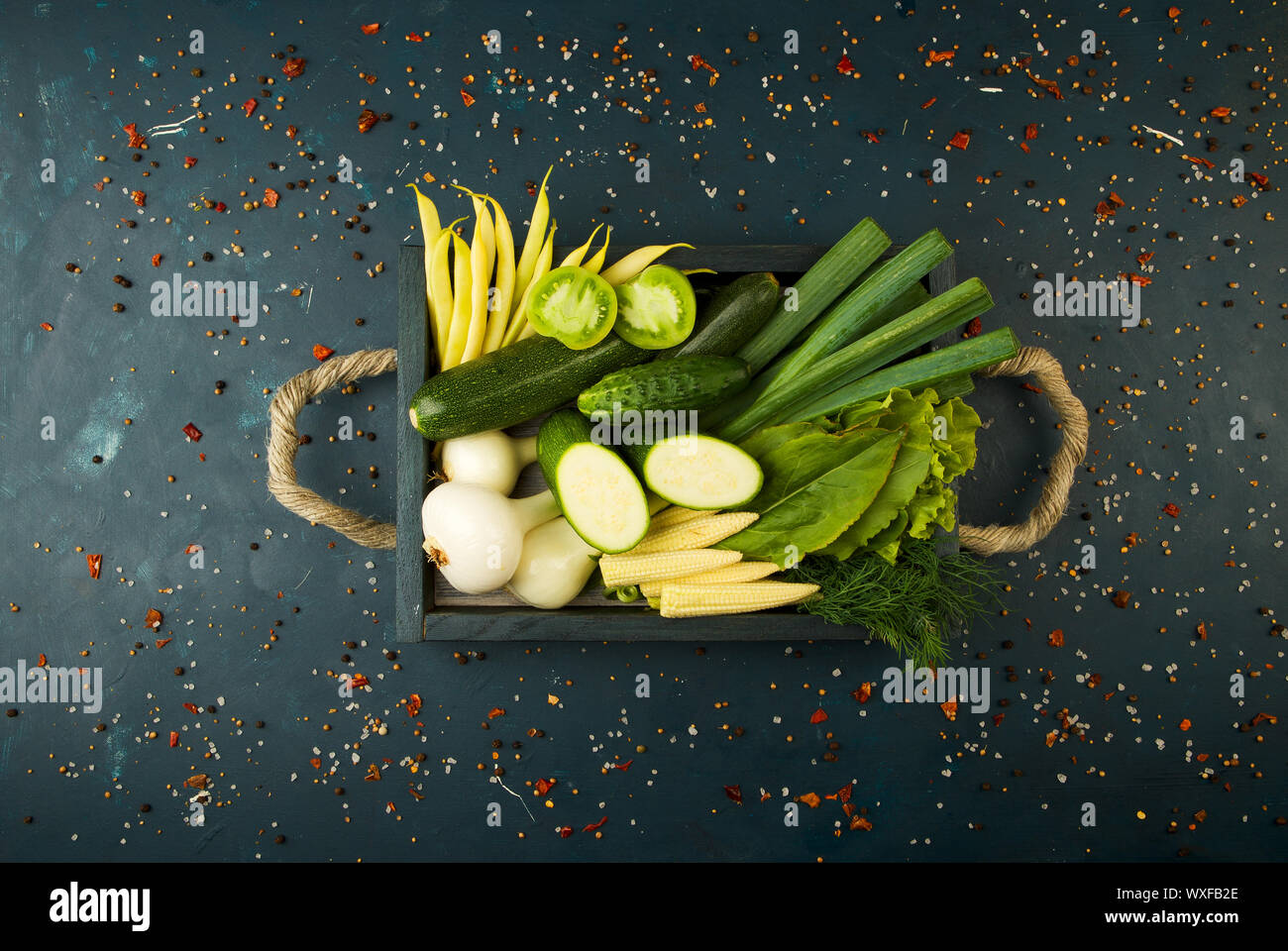 FRESH VEGETABLES ON WOODEN BOX ON A DARK STONE BACKGROUND. THE CONCEPT OF VINTAGE. THE YOUNG CORN ONIONS ASPARAGUS GREEN TOMATO Stock Photo