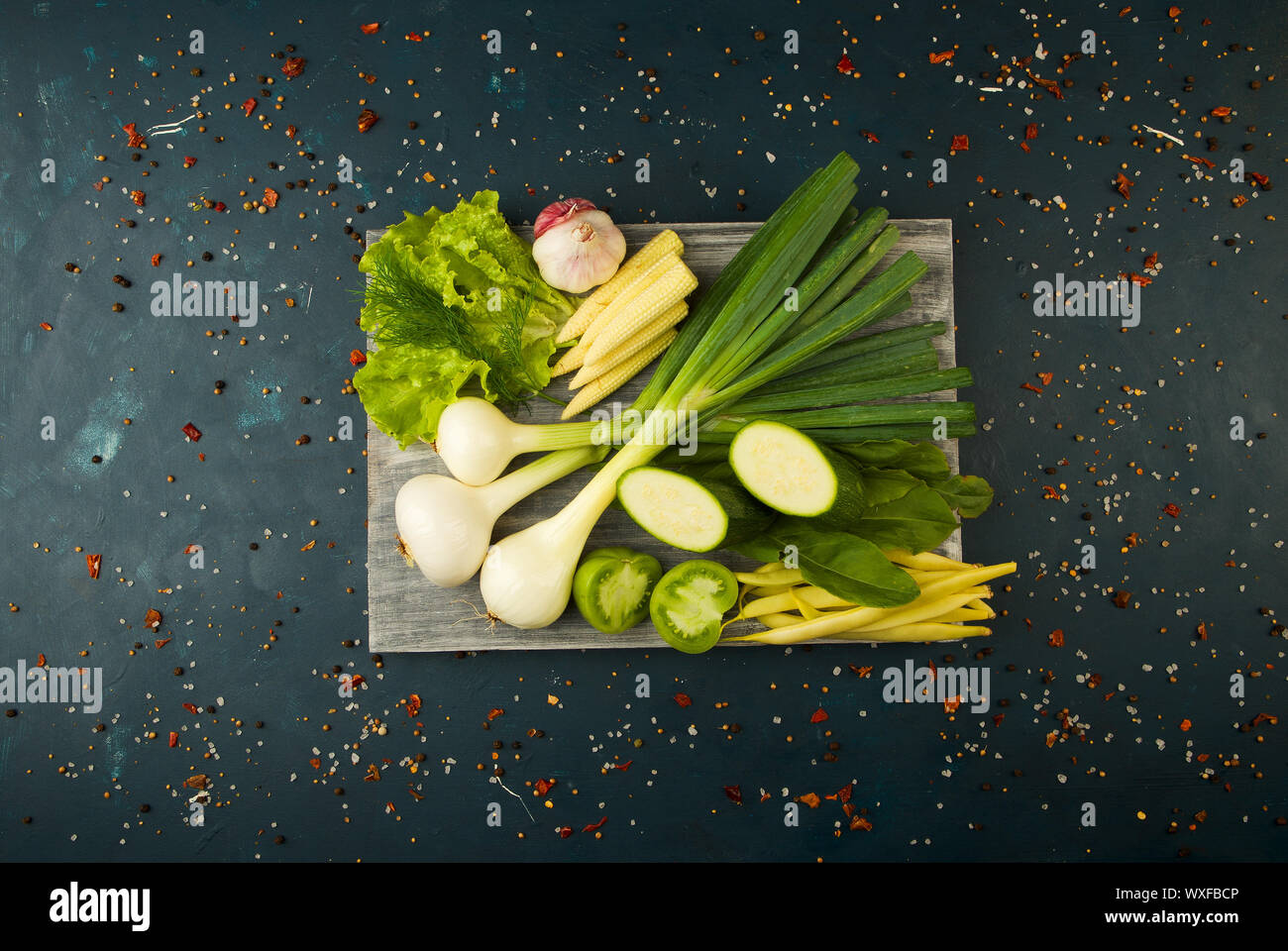 ONIONS GARLIC ON THE BOARD. GREEN ONIONS FEATHERS WITH THE HEADS OF GARLIC LYING ON A WOODEN BOARD ON A TEXTURED BACKGROUND. Stock Photo