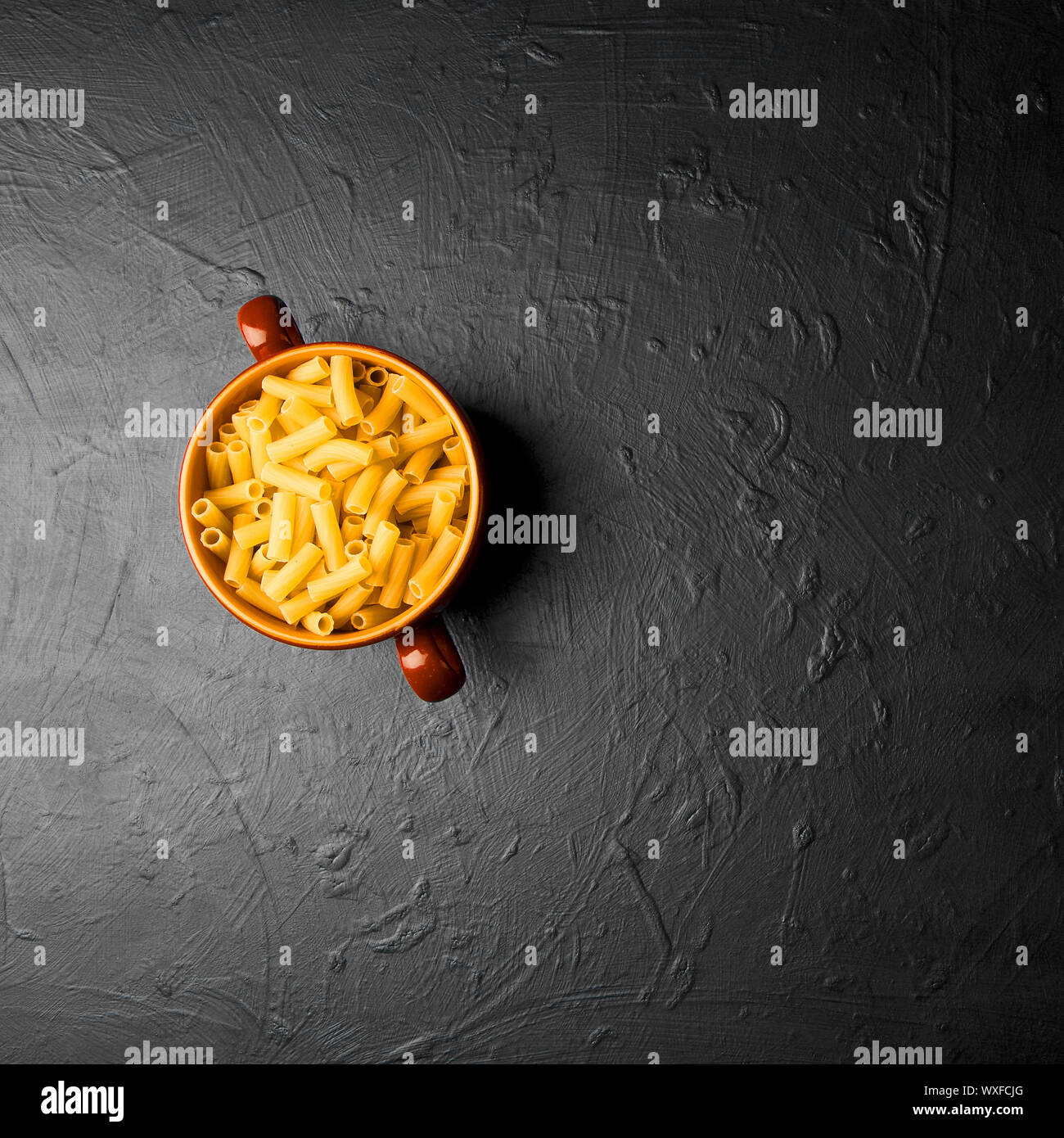 PASTA IN A PLATE ON A DARK BACKGROUND. YELLOW MACARONES IN CLAY BEAM ON DARK RELIEF BACKGROUND. Stock Photo