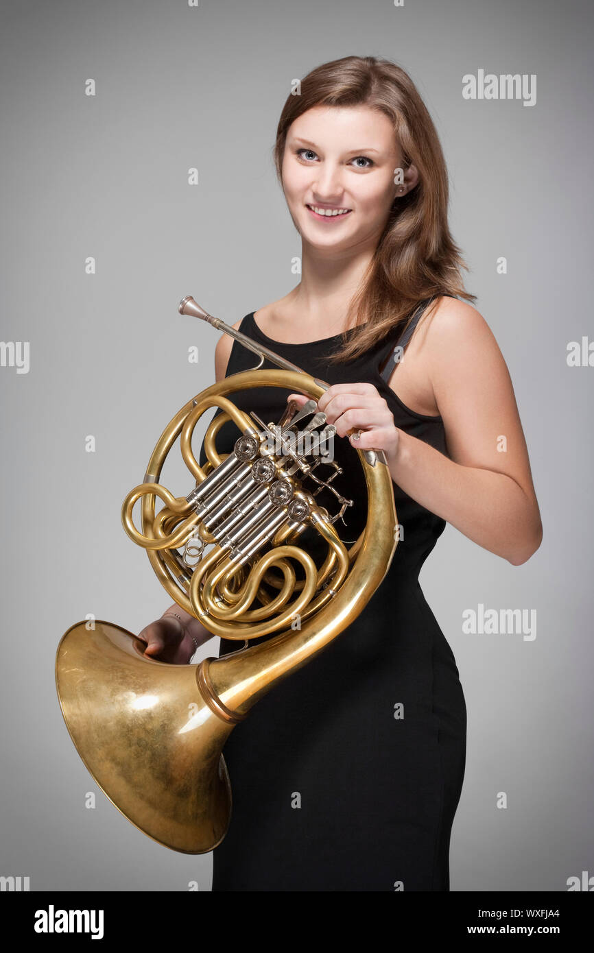 young female musician with concert french horn in black dress Stock